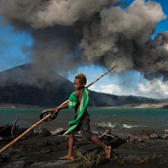 Tavurvur, Papua-Neuguinea  Munganau kennt nichts anderes als das  Leben mit dem Tavurvur. Seit­ dem er auf der  Welt ist, spuckt der Vulkan fast täglich Asche,  Lavabomben und lässt den Himmel nachts  leuchten.