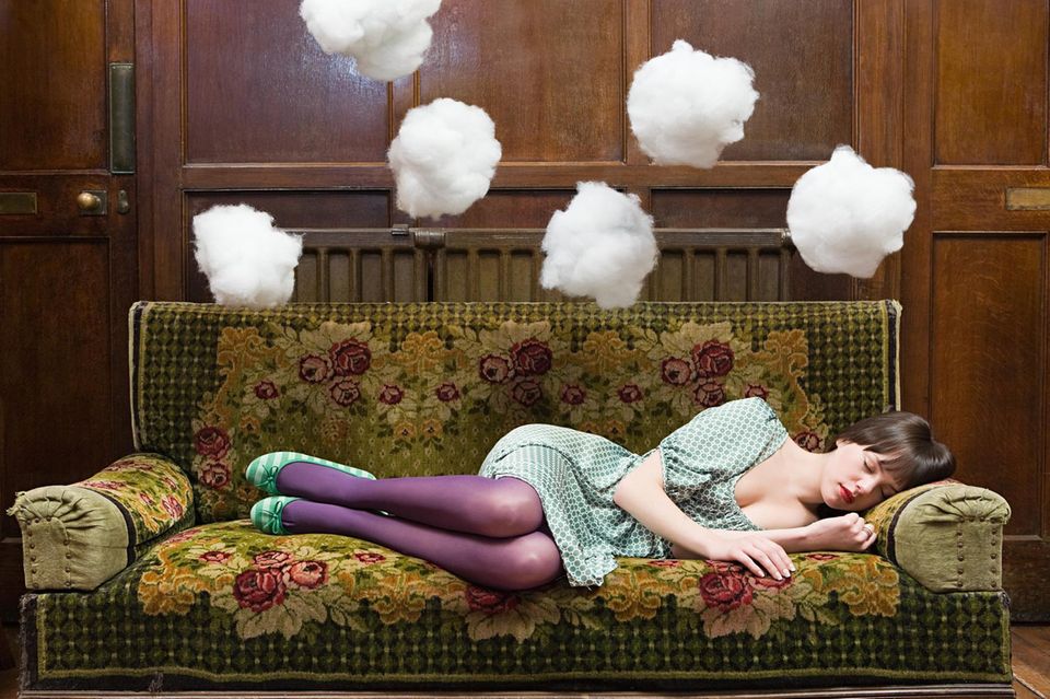 Eine Frau schläft auf dem Sofa, darüber schweben Wattewolken 1.5004