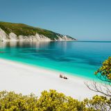 Amazing Fteri beach lagoon, Cephalonia Kefalonia, Greece. Tourists under umbrella relax near clear blue emerald turquise sea water. White rocks in background.
