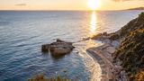 Versteckte Bucht am Mittelmeer zum Sonnenaufgang, der kleine Strand aus Sand und Kieselsteinen in den warmen Farben der Morgendämmerung, Blick auf das Meer am Xigia Sulfur Beach, Zakynthos, Ionische Inseln, Griechenland