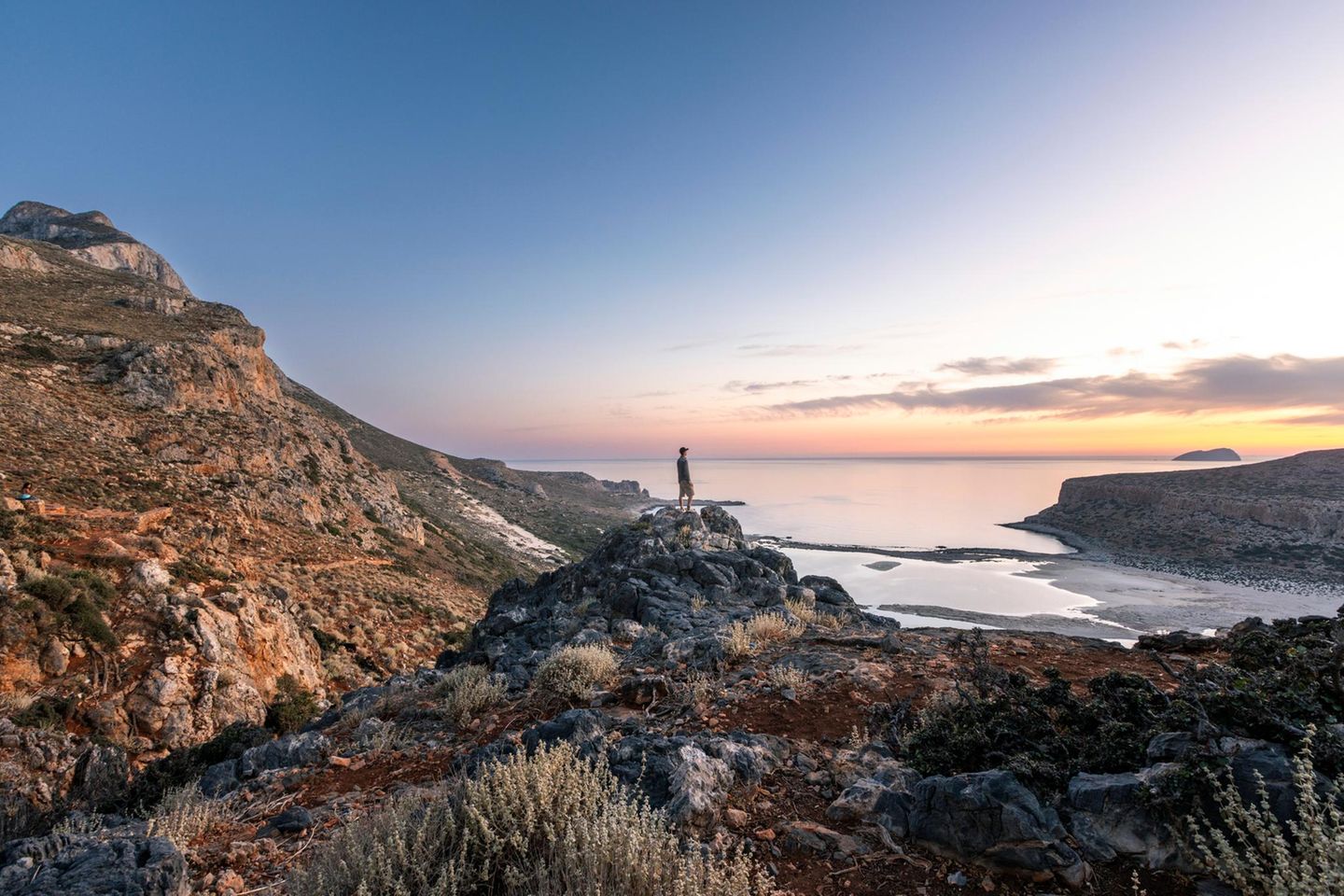 Kreta A person stands on a rock overlooking Balos Beach in Crete, Greece at sunset