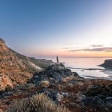 A person stands on a rock overlooking Balos Beach in Crete, Greece at sunset