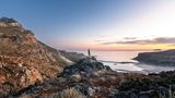 A person stands on a rock overlooking Balos Beach in Crete, Greece at sunset