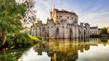 Die Gravensteen Burg ist in einem warmen Sommerlicht angestrahlt. Sie wirkt erhaben, eingebettet im Burggraben.