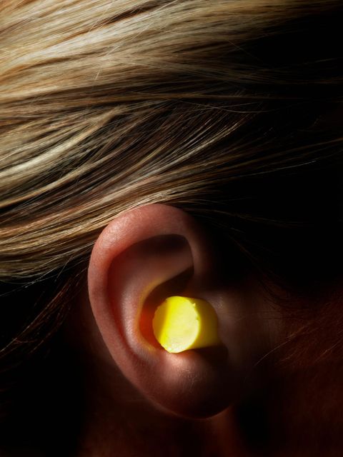 Nahaufnahme: Gelber Ohrstöpsel im Ohr einer blonden Frau.