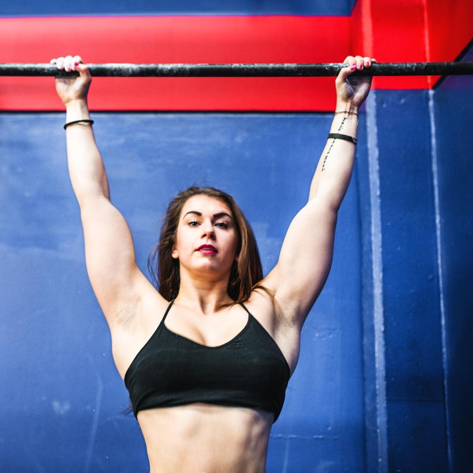 Eine Krafsportlerin hängt an einer Stange in einem Fitnesstudio