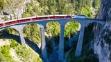 Drone shot of train passing the Landwasserviadukt near Filisur, red train of Bernina Express, Switzerland