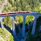 Drone shot of train passing the Landwasserviadukt near Filisur, red train of Bernina Express, Switzerland