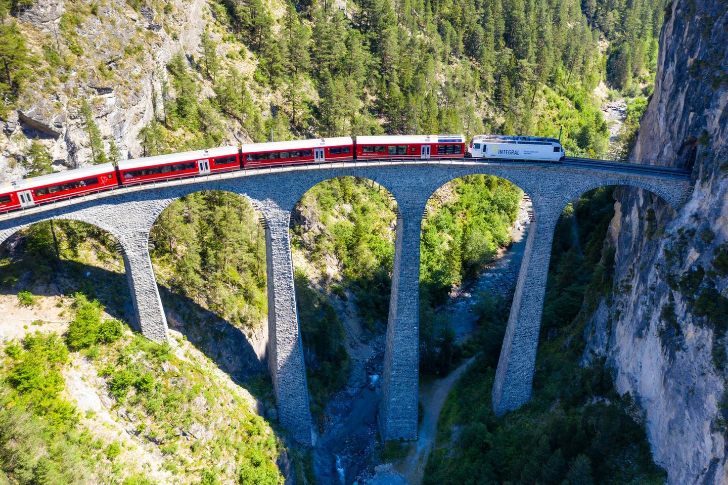 Drone shot of train passing the Landwasserviadukt near Filisur, red train of Bernina Express, Switzerland