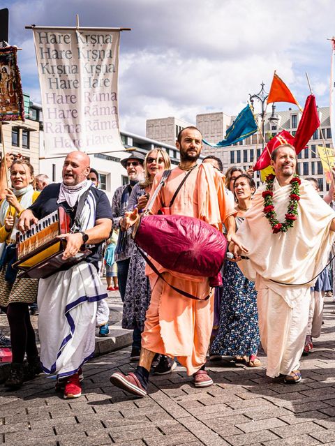 musizierende Menschen mit bunten Gewändern und Hare Krishna Fahnen