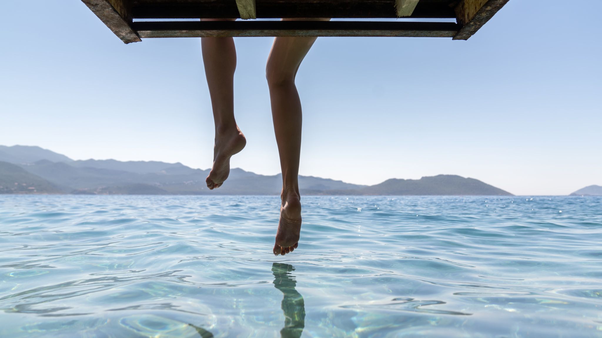 Frau auf einem Steg lässt die Beine baumeln