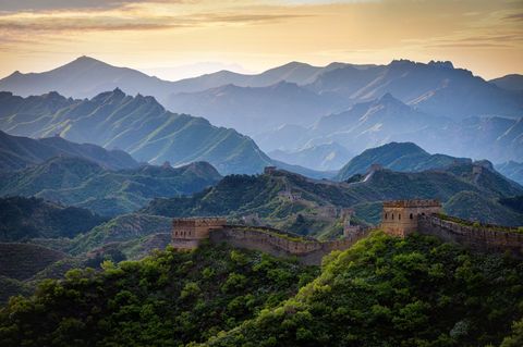 Die Chinesische Mauer zieht sich über einen bewaldeten Höhenzug im Licht des beginnenden Tages