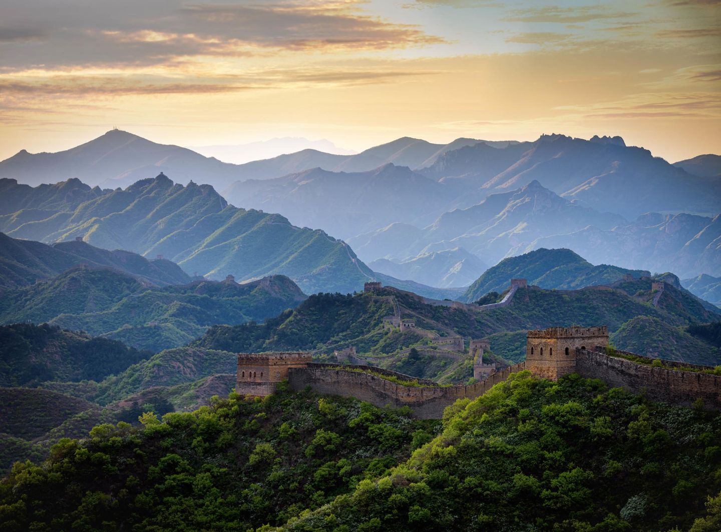 Die Chinesische Mauer zieht sich über einen bewaldeten Höhenzug im Licht des beginnenden Tages