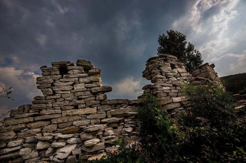 Reste einer Mauer aus Natursteinen vor einem dramatisch dunklen Wolkenhimmel