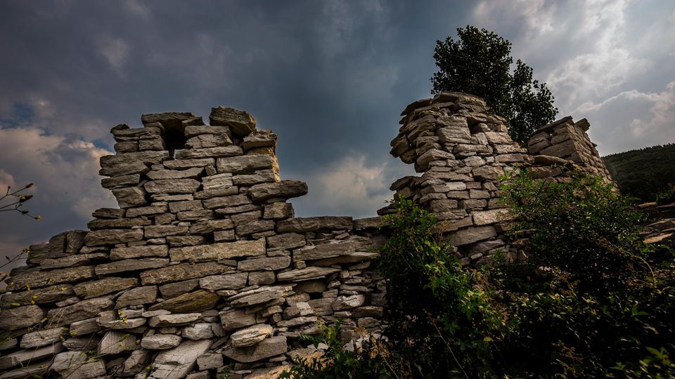 Reste einer Mauer aus Natursteinen vor einem dramatisch dunklen Wolkenhimmel