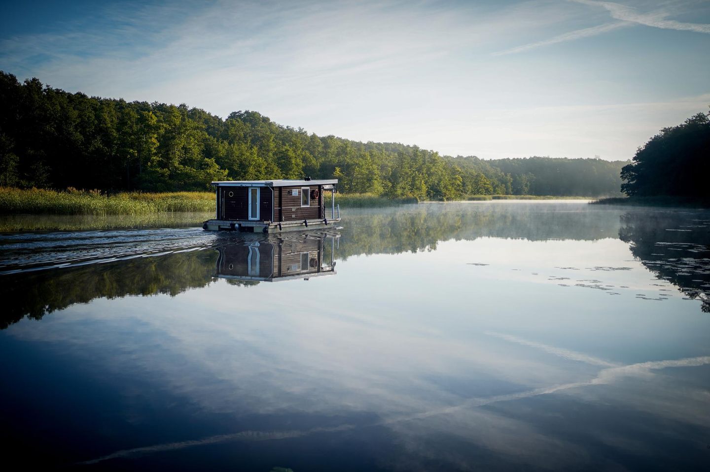 Schönes Revier in Brandenburg: Ein Hausboot fährt am frühen Morgen im Sonnenschein über die Havel
