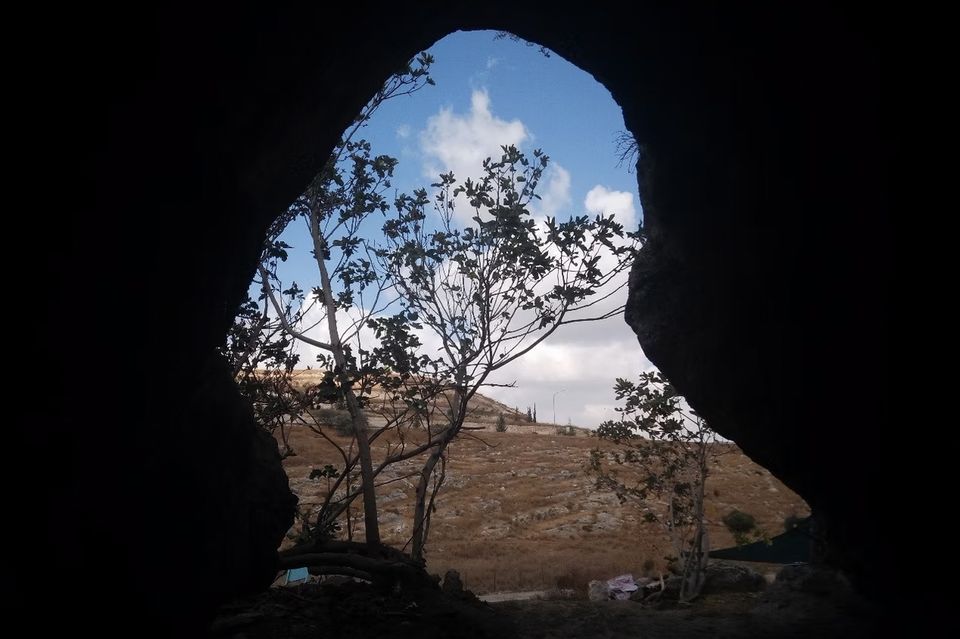 Blick aus einer dunklen Höhle in Israel ins Freie, auf eine karge Ebene und Himmel 1.3326