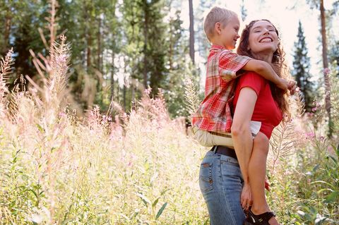 Glückliche Mutter mit Kind auf den Schultern im Wald in Finnland