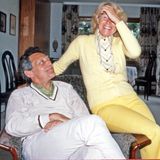 Mann in einem Wohnzimmersessel, auf dessen Lehne sitzt eine lachende Frau