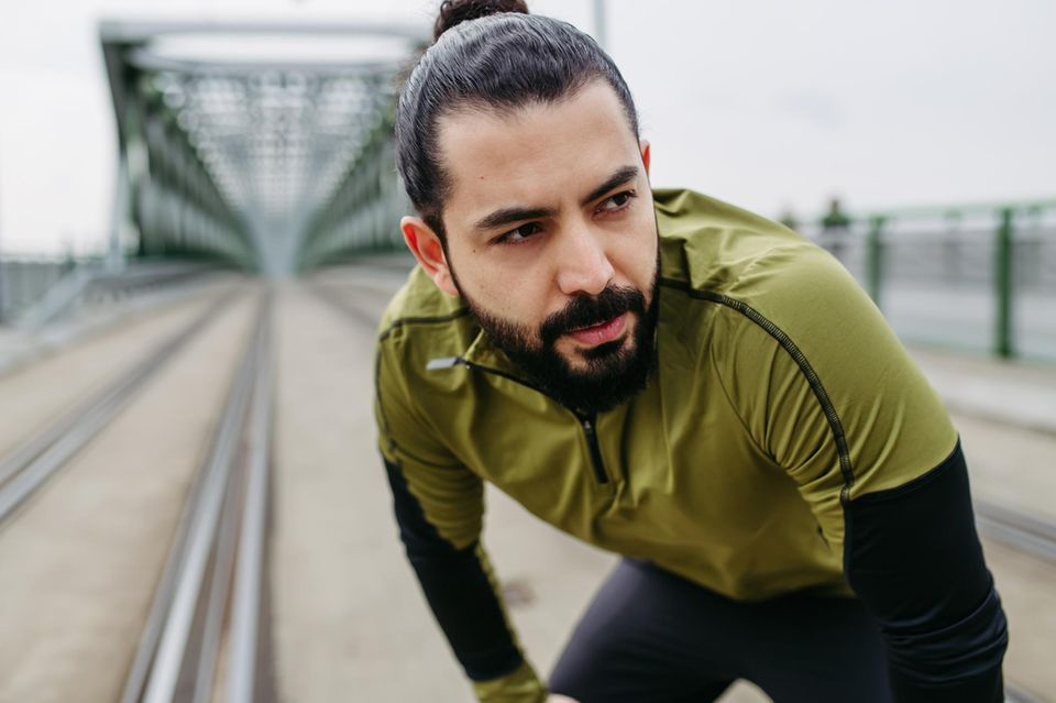 Ein Mann in Sportkleidung stützt sich auf seine Knie und bereitet sich womöglich auf einen Marathon vor 1.5004