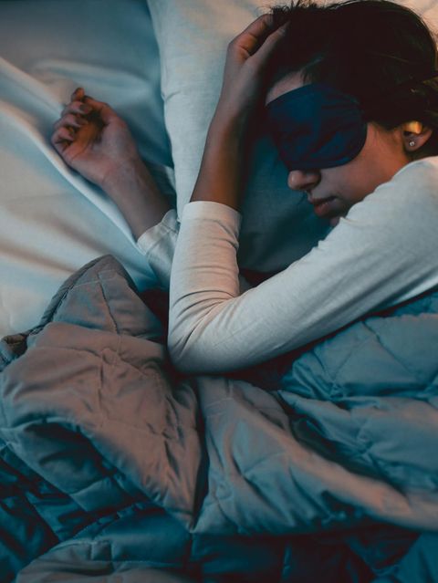 Frau im Bett mit Schlafmaske und Ohrenstöpseln