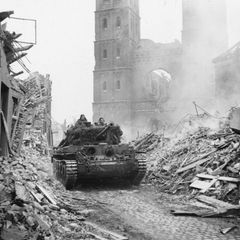 Ein Panzer fährt in einer Stadt zwischen Trümmern hindurch