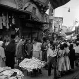 Atatürk will auch die türkische Wirtschaft auf das Niveau westlicher Industriestaaten hieven, lässt Fabriken errichten und Maschinen kaufen. Doch der Rückstand der agrarischen und in vielen Regionen extrem strukturschwachen spätosmanischen Ökonomie ist nicht so schnell aufzuholen. In dieser Ladenstraße ist 1951 das Angebot an Kleidung reichhaltig, das Händler teils auf Tischchen und auf dem Boden ausgelegten Decken zeigen. Viele Geschäftsleute halten an alten Gewohnheiten fest, teils aus Überzeugung, teils aus Mangel an Geld oder Alternativen.