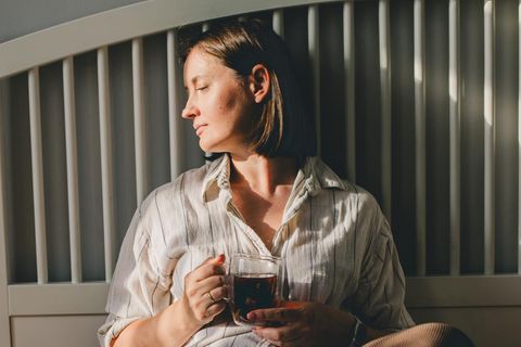 Frau sitzt auf dem Bett und trinke Kaffee