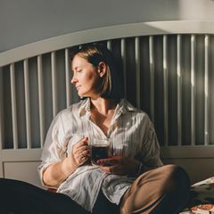 Frau sitzt auf dem Bett und trinke Kaffee