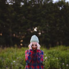 Junge Frau steht in der Natur und hält sich den Kopf