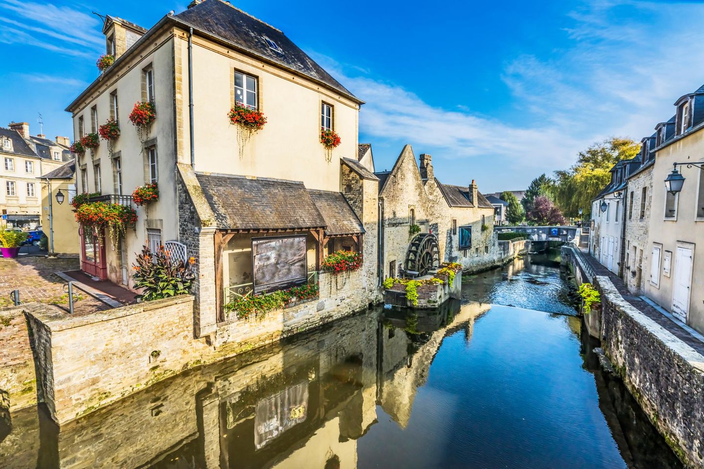 Blick auf Häuser in der Ortschaft Bayeux. Im Vordergrund Wasser