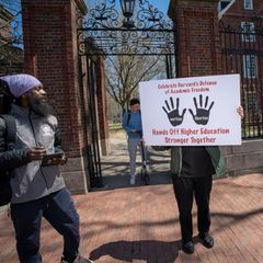 vier Menschen vor der Harvard Universität von denen einer ein Schild hochhält