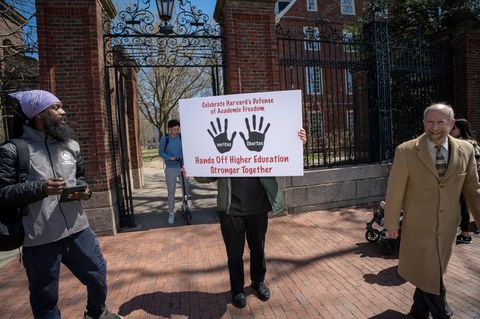 vier Menschen vor der Harvard Universität von denen einer ein Schild hochhält