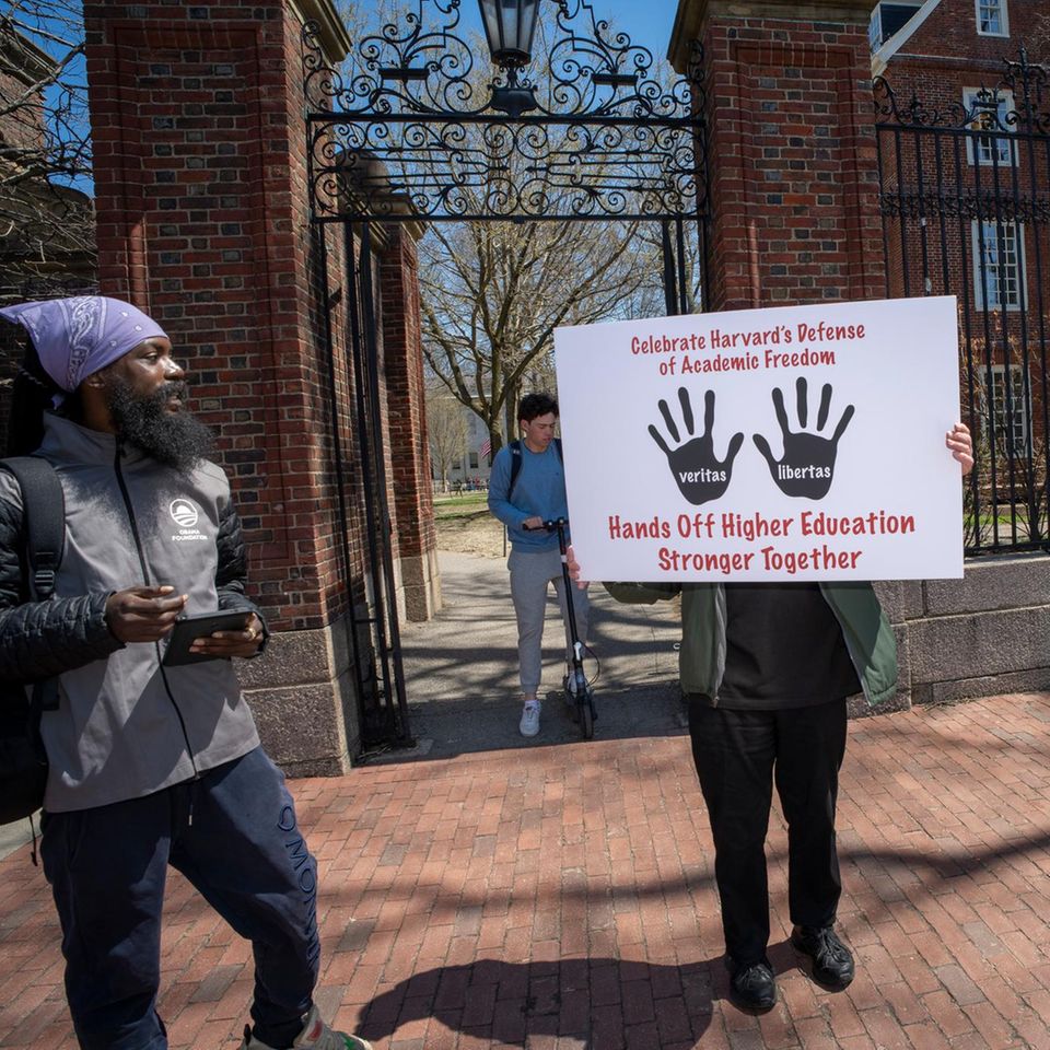 vier Menschen vor der Harvard Universität von denen einer ein Schild hochhält