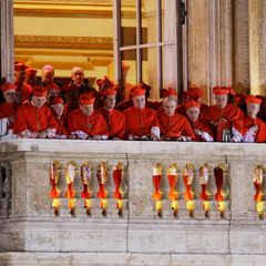 Während sich Papst Franziskus 2013 kurz nach seiner Wahl zum ersten Mal der Öffentlichkeit zeigt, stehen auf einem benachbarten Balkon Kardinäle zusammen und verfolgen die Reaktion auf ihre überraschende Wahl