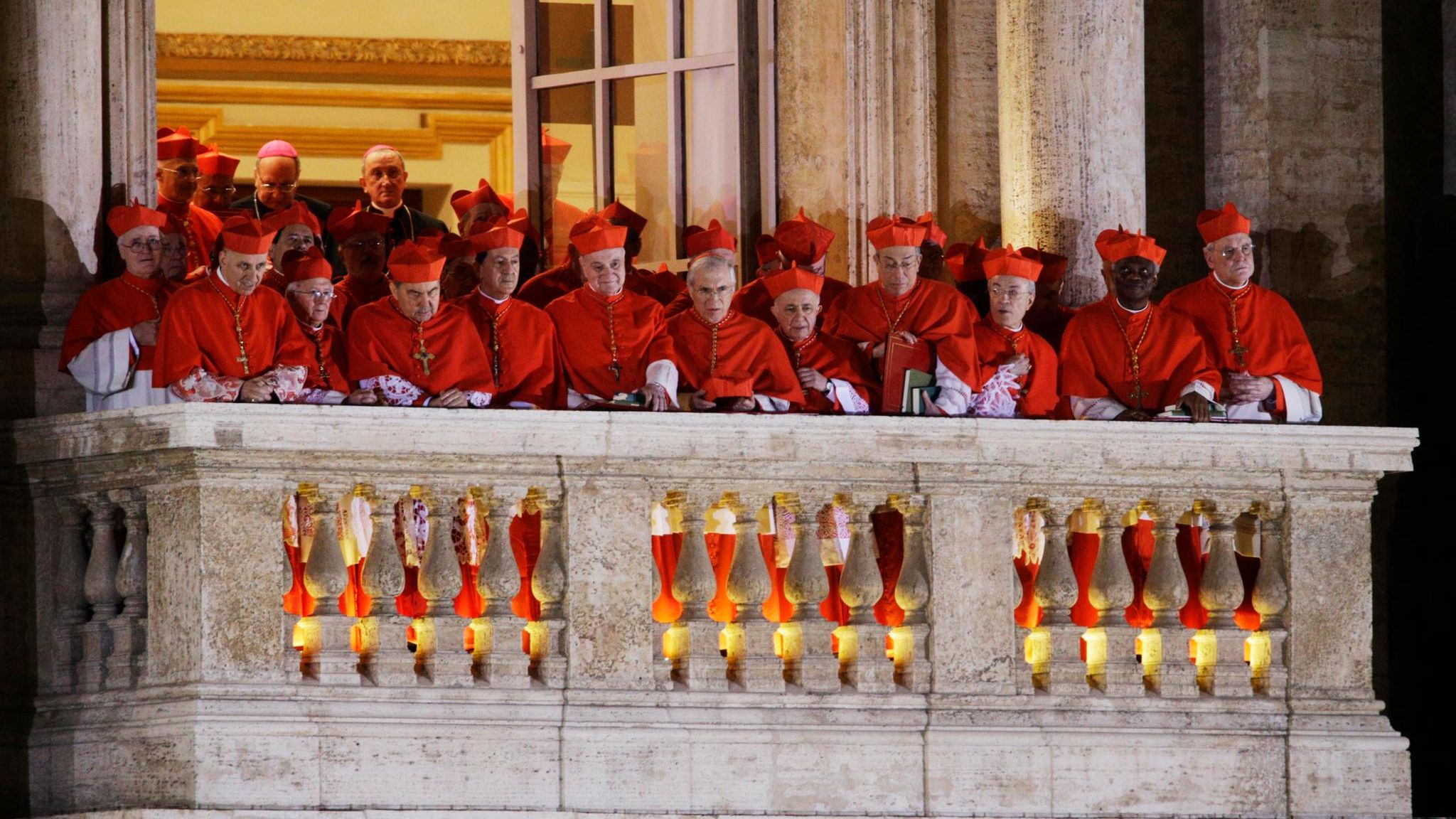 Während sich Papst Franziskus 2013 kurz nach seiner Wahl zum ersten Mal der Öffentlichkeit zeigt, stehen auf einem benachbarten Balkon Kardinäle zusammen und verfolgen die Reaktion auf ihre überraschende Wahl
