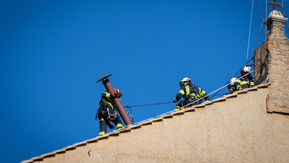 Feuerwehrleute bringen auf dem Dach der Sixtinischen Kapelle den Schornstein an, auf den die Weltöffentlichkeit in den kommenden Tagen gespannt blicken wird