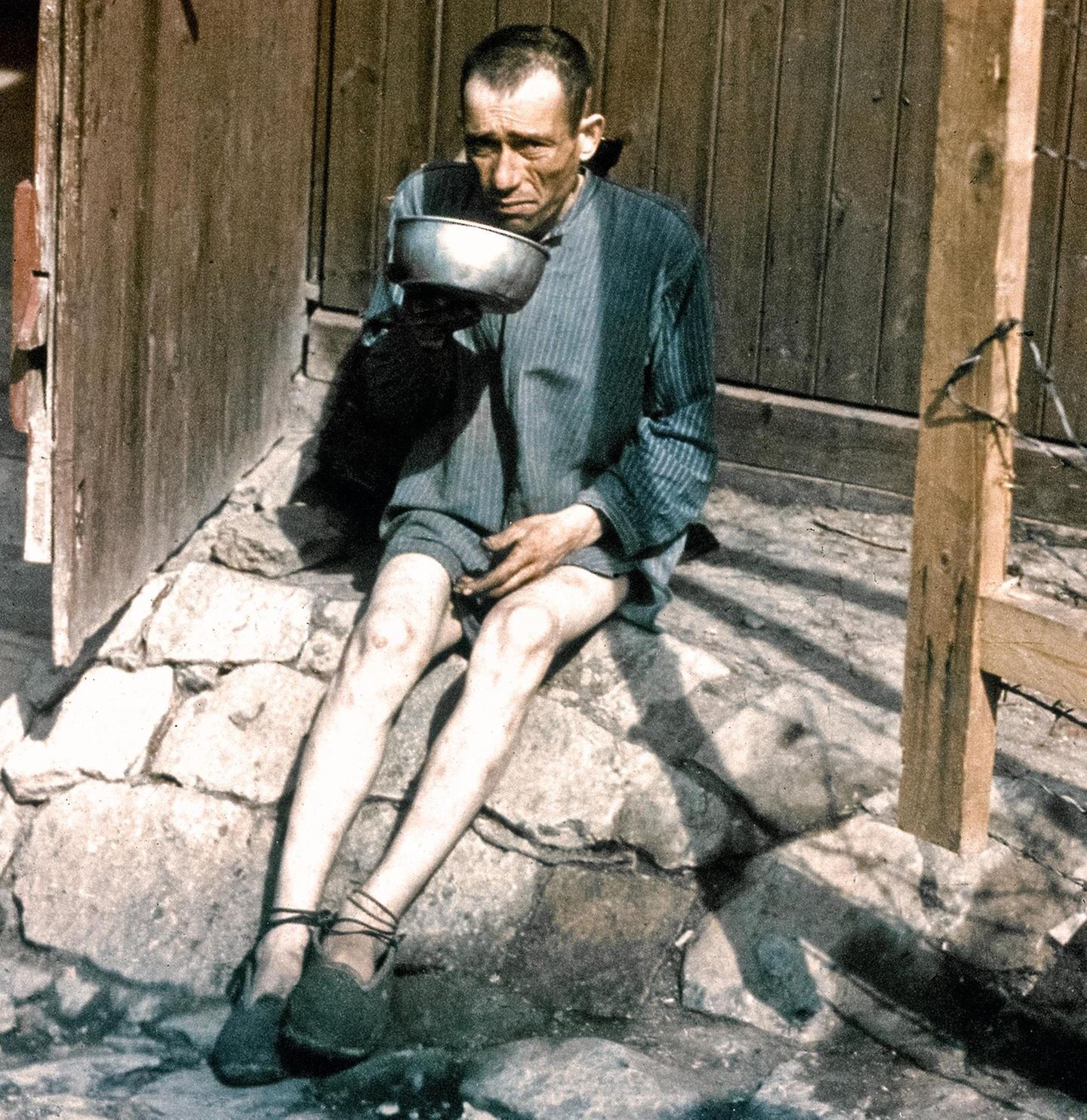 Ein befreiter KZ- Insasse in Buchenwald sitzt erschöpft am Boden