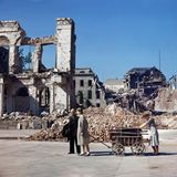 Menschen schieben Karren durch zerbombte Straße