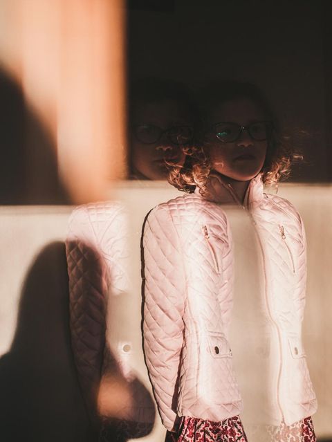 Ein Mädchen steht vor einer Wand, ihr Gesicht ist von einem Schatten bedeckt