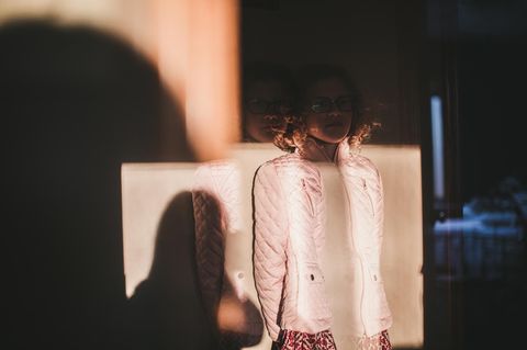 Ein Mädchen steht vor einer Wand, ihr Gesicht ist von einem Schatten bedeckt