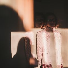 Ein Mädchen steht vor einer Wand, ihr Gesicht ist von einem Schatten bedeckt