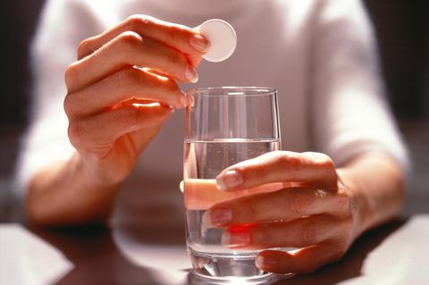 Eine Frau hält eine Brausetablette über ein Glas