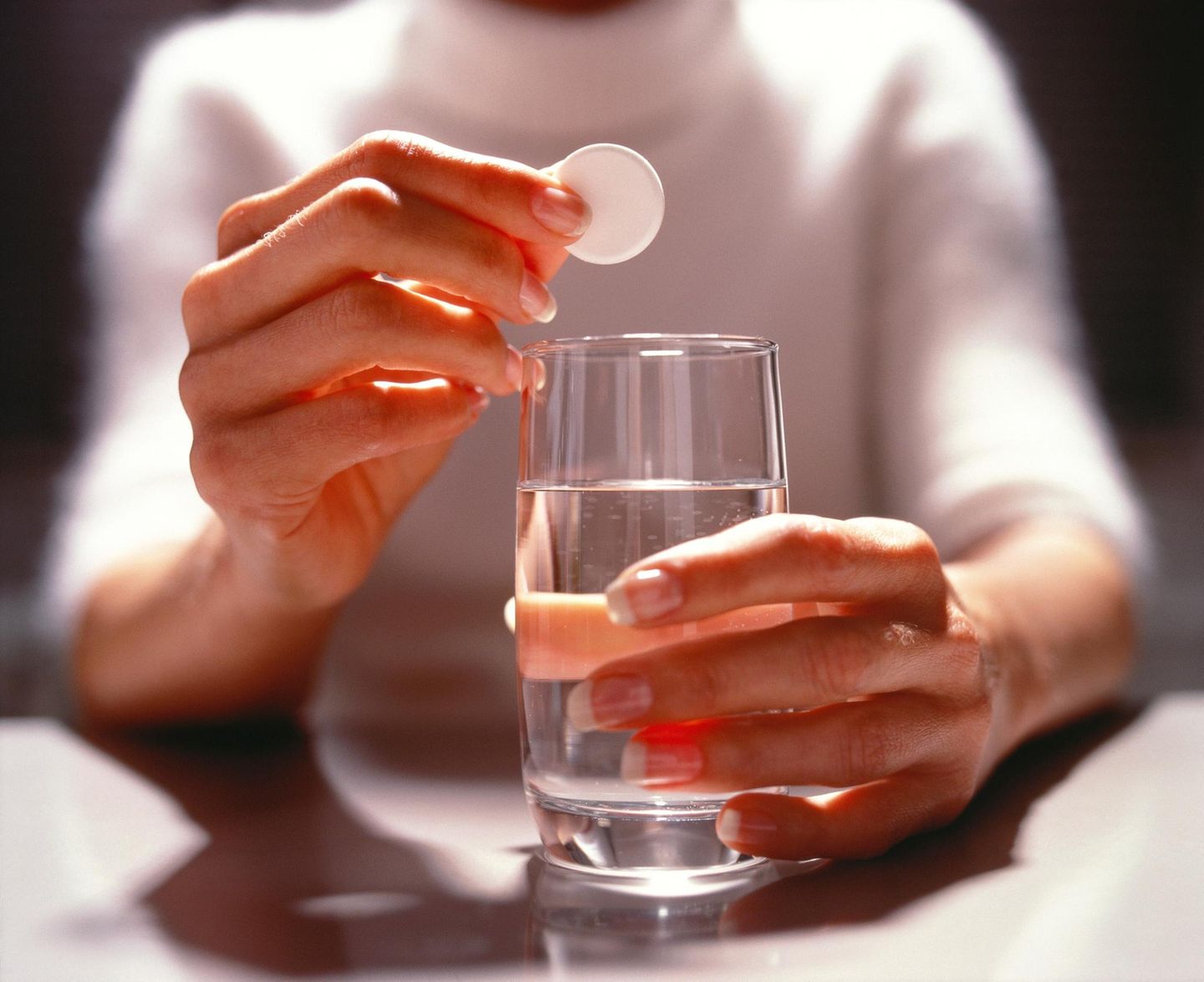 Eine Frau hält eine Brausetablette über ein Glas