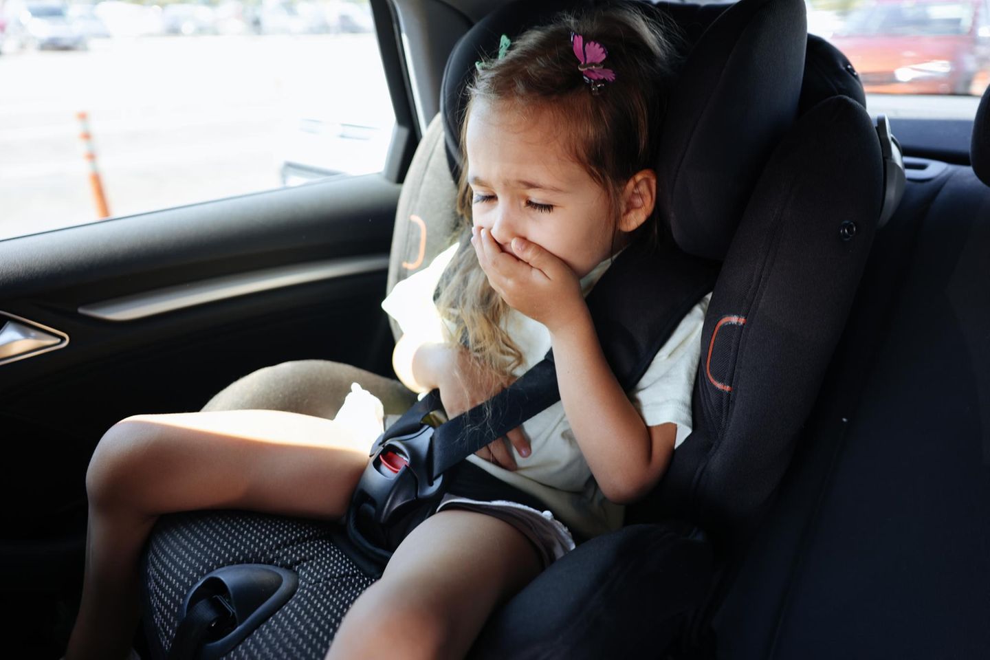 Kleines Mädchen im Auto hält sich die Hand vor den Mund