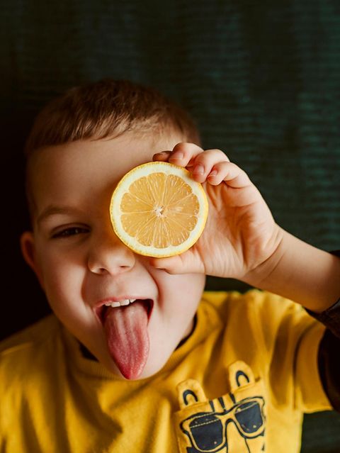Junge hält sich eine Zitronenscheibe vors Auge und steckt die Zunge raus