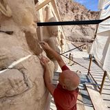 Ein Bildhauer auf einem Baugerüst ergänzt den Bart einer Osirisstatue der Hatschepsut