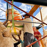 Männer führen den in bunten Gurten hängenden Statuenkopf an die richtige Positon