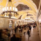 Menschen strömen durch eine Bahnsteighalle mit gelbem Tonnengewölbe und weißem Stuck