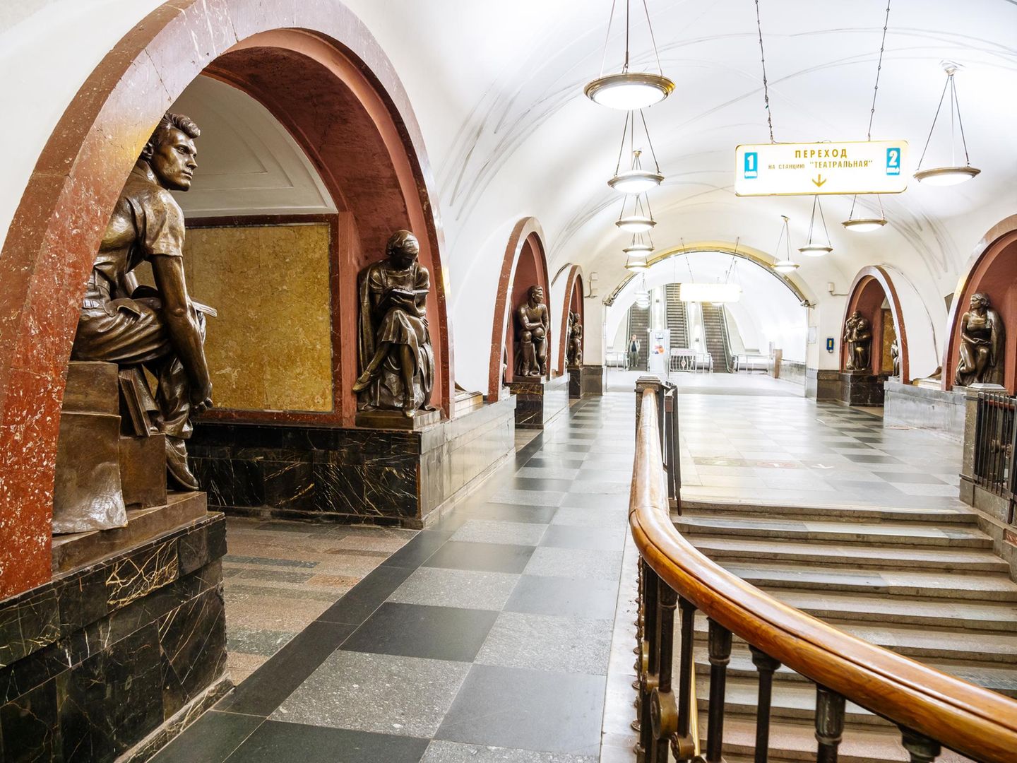 Bahnsteighalle mit Treppen, Kronleuchtern und von Statuen gesäumten, steinernen Rundbögen